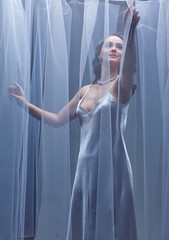 Portrait of a young female covered with veil. Woman is dressed in a peignoir and wears a necklace and earrings.