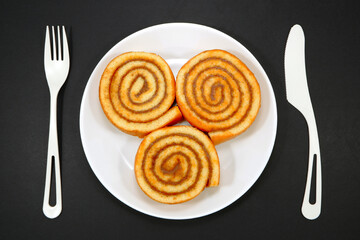 Roll cakes together on white plate with cutlery set on black background flat lay photography 