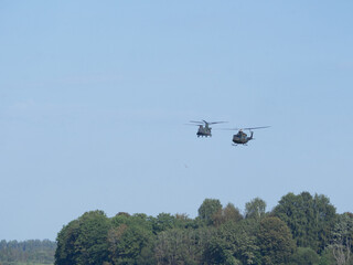 Two military helicopters fly above the treetops. NATO military exercises. Threat of war in Europe