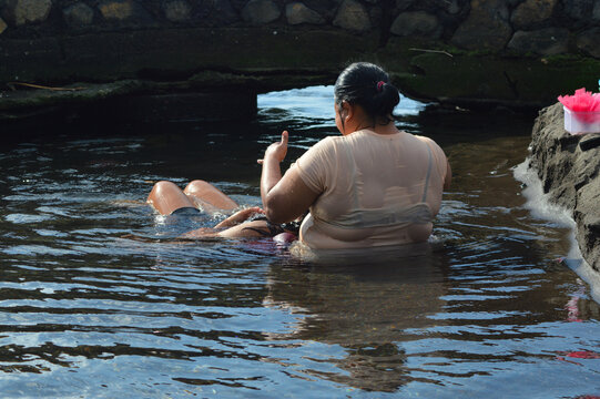 A daughter lies back resting her head on her motherâ€™s lap while they sit immersed in a shallow brackish creek beside the sandy shoreline, enjoying a tender beachside moment. - Powered by Adobe