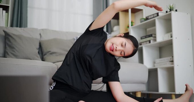 Handheld low angle view shot, Healthy Asian woman practicing yoga poses online on laptop in living room at home. Healthy lifestyle. Women Lifestyle