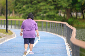 A back view Asian woman exercising in a park with a water bottle, being resilient, being...