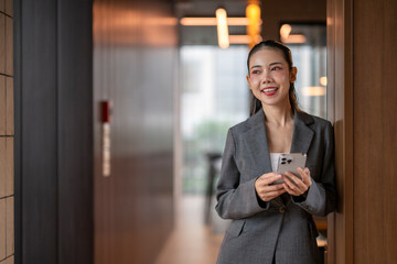 Smiling businesswoman using smartphone in modern office corridor