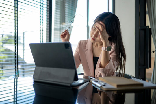 Young asian businesswoman having headache while working on a tablet in office