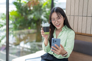 Smiling asian businesswoman using smartphone and drinking iced matcha green tea latte in cafe