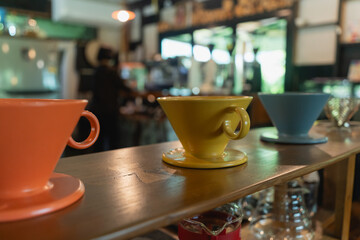 Colorful Ceramic Drippers on Wooden Shelf in Cozy cafe Setting with Blurred Barista in Background Creating Warm Atmosphere for Coffee Lovers