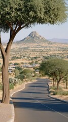 Obraz premium Scenic Road Through Arid Landscape with Mountain Backdrop, Village, and Trees