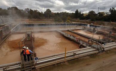 Paper manufacturing- workers stand on the walkway over the mixing-pulp pond as the mixture churns. Albury-New South Wales. 