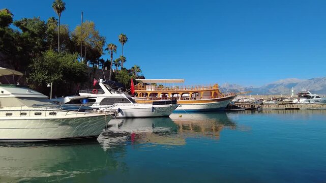4K Tour boats docked at Kaleici Marina in Antalya, floating on the calm Mediterranean waters with cliffs and mountains in the distance. Copy space available at the top