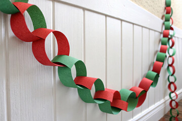 Colorful paper chain garland in red and green interlocking circles hanging along white wainscoting for cheerful holiday decor.