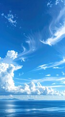 Serene vertical view of a bright blue sky with wispy clouds above a shimmering sea and distant, hazy islands