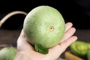 Fresh Shandong Emerald Melon in Hand with Mint Leaf on White Background - Small Green Asian Honeydew Fruit © HoangVan