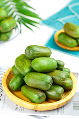 Fresh Mini Kiwi Berries in Wooden Bowl with Tropical Palm Leaves Background