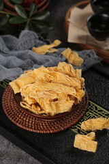 Dried tofu skin bean curd sheets in rustic wooden bowl on dark slate background for Asian vegetarian cuisine cooking