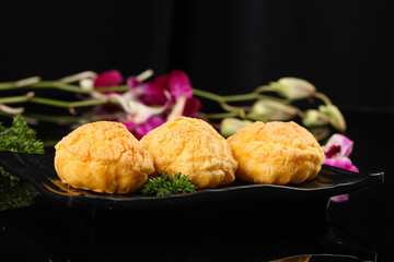 Crispy Golden Fried Puff Balls with Fresh Herbs and Orchid Flowers on Dark Elegant Plate
