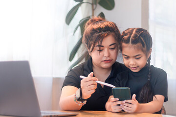 Mother teaches daughter how to use smartphone while sitting at home during the day