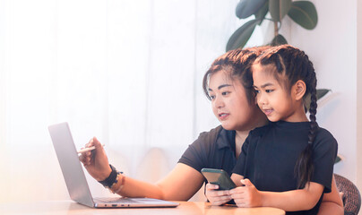 Mother and daughter work together on digital projects at home during afternoon hours