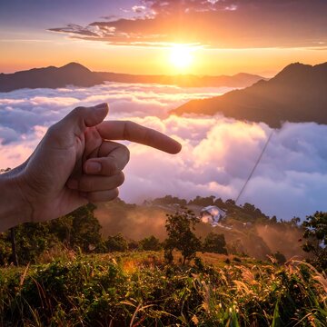 Hand pointing to a sunrise over a mountain landscape shrouded in clouds