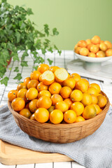 Fresh Kumquats in Wicker Basket on Rustic Kitchen Table with Natural Green Background