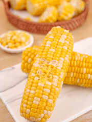 Fresh Sweet Corn Cobs with Golden Yellow Kernels on White Plates and Wicker Basket