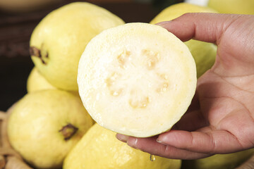 Fresh Guava Fruit Slice Held in Hand Showing White Creamy Interior with Soft Background
