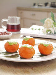 Fresh Persimmons on Plate with Tea and Dumplings in Kitchen Setting for Autumn Festival Celebration