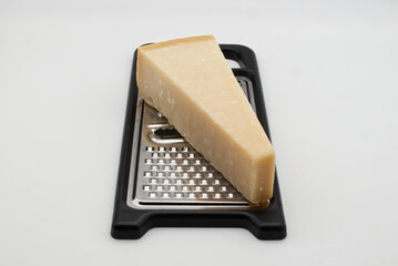 A delicious wedge of hard parmesan cheese rests on a kitchen grater, ready for culinary use.