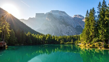 Tranquil turquoise lake surrounded by a dense evergreen forest and towering mountains under a bright, sunlit sky, creating a serene natural vista