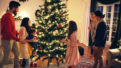 Family decorating a Christmas tree in a cozy living room at night while enjoying festive holiday spirit