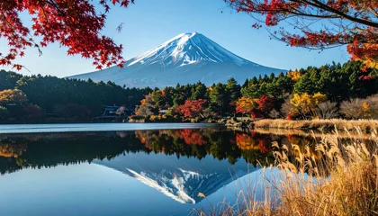 Wanddecoratie Reflectie Snow-capped mountain reflected in calm lake, framed by autumn foliage in warm hues, offering a serene and picturesque vista of nature  © Juan