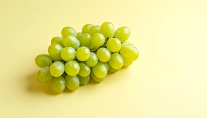 A lush bunch of vibrant green grapes are placed against a pale yellow background.