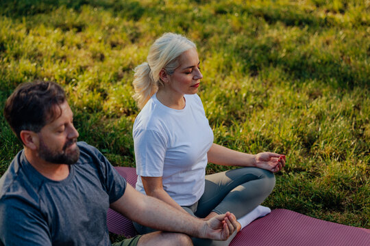 Senior couple practicing yoga and meditating outdoors on yoga mat
