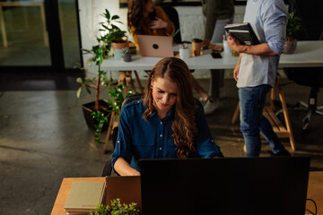 Focused employee working on computer in busy office with colleagues collaborating