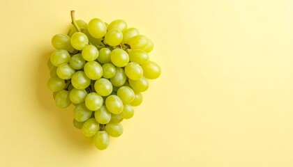 A vibrant bunch of fresh, green grapes artfully displayed on a yellow background surface.