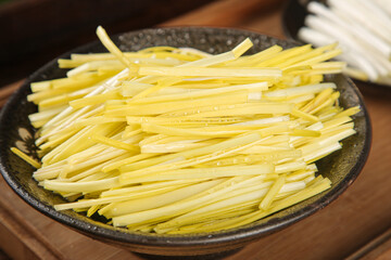 Fresh sliced leeks in black bowl ready for cooking - white and green vegetable strips on wooden background