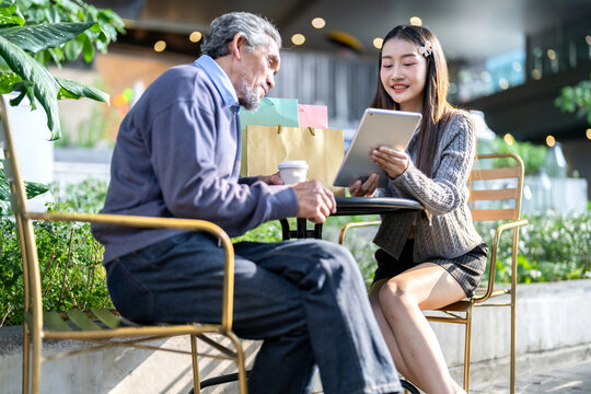 Asian young woman showing tablet to senior man while smiling at cafe, multigenerational bonding, digital learning relaxing time, family connection, technology sharing lifestyle, happy interaction