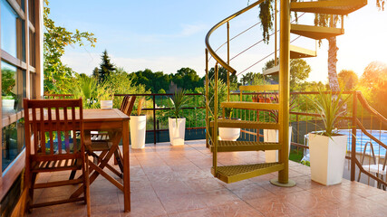 Steel spiral gold staircase on the terrace with plants and plants in pots background.