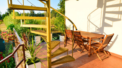 Steel spiral gold staircase on the terrace with plants and plants in pots background.