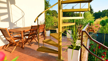 Steel spiral gold staircase on the terrace with plants and plants in pots background.