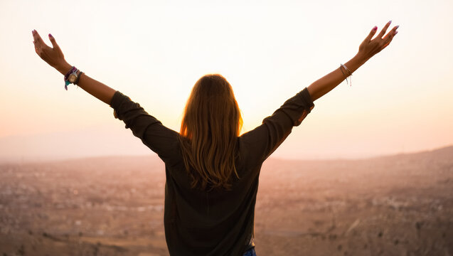 Woman is standing on a hill and is holding her arms up in the air