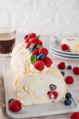 Meringue Pavlova roll cake with cream and fresh berries on top on a ceramic board on a concrete background. Copy space.