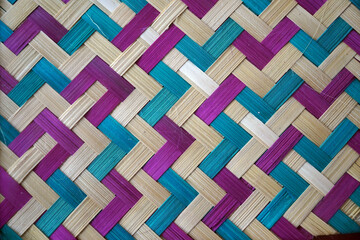 A colorful woven mat with a beautiful herringbone pattern, made from dyed bamboo or rattan, showcasing traditional Asian craft and serving as a vibrant abstract background.