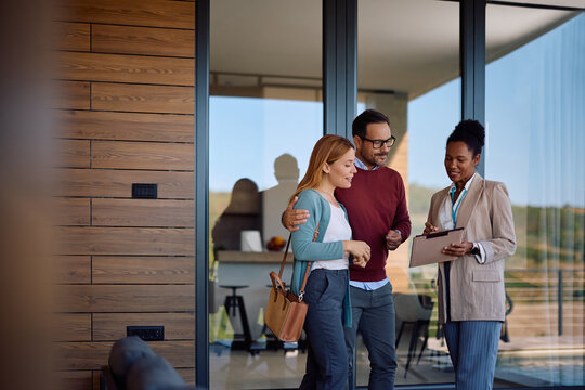 Smiling couple and their real estate agent analyzing paperwork during open house day.