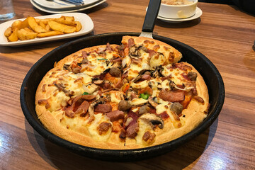 Close-up photo of a pizza in a black pan with a handle, cut into several slices