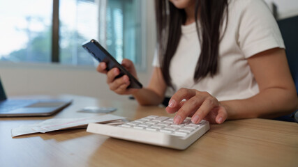 Financial Management. Young woman using smartphone and calculator for budgeting.