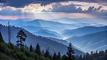 Obraz premium Majestic mountain ranges bathed in ethereal blue hues, with sunbeams piercing through dramatic clouds and evergreen trees dotting the rolling hills below.