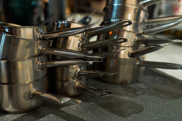 Stacked stainless steel saucepans arranged on countertop, handles pointing outward, reflecting kitchen environment, cookware organized for storage or preparation in commercial kitchen
