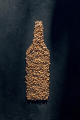 Symbol of a naturally made bottled drink, the raw material for which is wheat grain. The shape of a bottle, made of wheat grain on a black background.