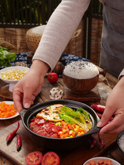 Hands presenting healthy rice casserole with fresh vegetables on rustic wooden table - homemade comfort food cooking