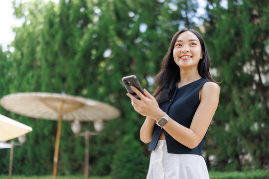 Smiling businesswoman using smartphone in a green park - Powered by Adobe